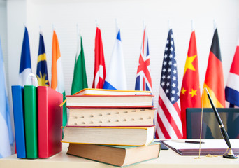 A pile of books on desk with calendar yearly planner over national flags cloth on poles background, Stacked of textbook with planner write meeting agenda for organizer to plan timetable against flags 