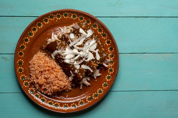Mexican chicken enchiladas with mole sauce and rice on turquoise background