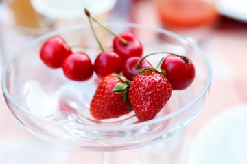 Strawberries and cherries are in a crystal vase
