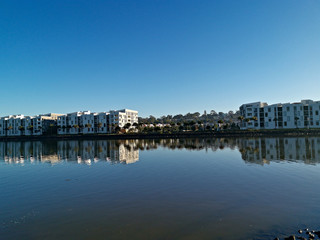 Fototapeta na wymiar Beautiful view of a river with reflections of modern apartment buildings, deep blue sky and trees on water, Parramatta river, Wilson Park, Silverwater, Sydney, New South Wales, Australia 