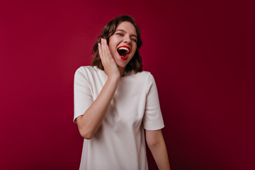 Enthusiastic laughing girl in white outfit chilling in studio. Blissful female model with dark hair smiling during photoshoot.