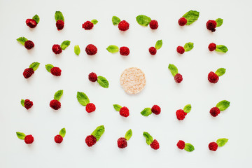 Rice cracker surrounded by a pattern of raw raspberries and mint leaves