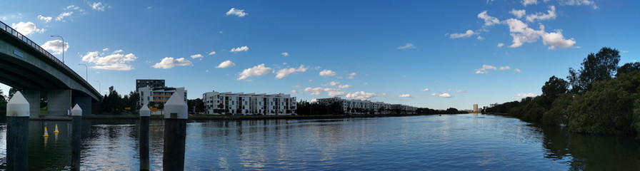 Fototapeta premium Beautiful panoramic view of a river with reflections of modern apartment buildings, deep blue sky and trees on water, Parramatta river, Wilson Park, Silverwater, Sydney, New South Wales, Australia 