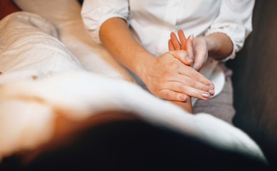 Caucasian lady lying and having hand massage procedure covered with a white towel at spa center