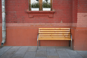 wooden bench against a brick wall of a house with a window