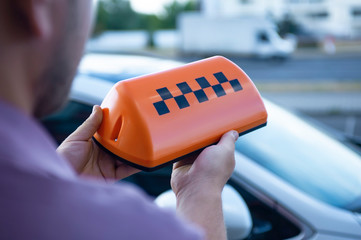Orange sign of a taxi in the hands of a man on the background of a car. The driver went to work.