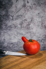 Weird tomato fights the knife on a wooden cutting board