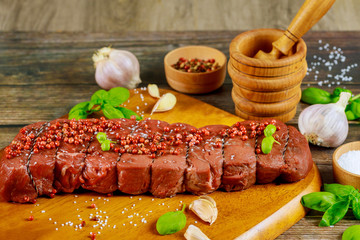Raw beef fillet with herbs and spices on wooden board.