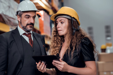 Engineer woman and businessman wearing a hardhat standing cargo at goods warehouse and check for control loading from Cargo freight ship for import and export by report on tablet. Teamwork concept