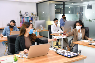 Asian office workers wearing face masks working in new normal office and doing social distancing during corona virus covid-19 pandemic