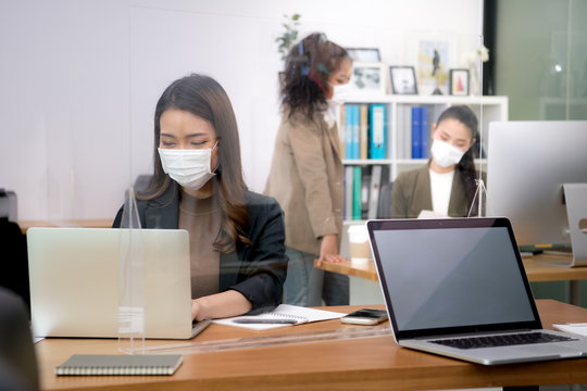 Asian Office Workers Wearing Face Masks Working In New Normal Office And Doing Social Distancing During Corona Virus Covid-19 Pandemic