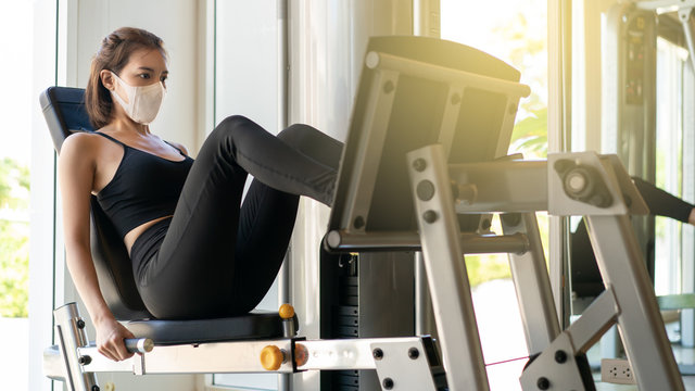 Woman wearing face mask exercising with leg press machine in gym. during corona virus pandermic.