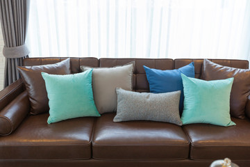 Modern living room with big comfortable leather sofa with green and black pillows on it.