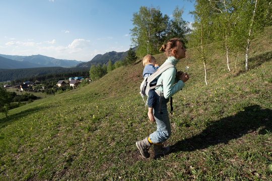 Woman carrying kid in a children's backpack walking outdoor in summer mountains