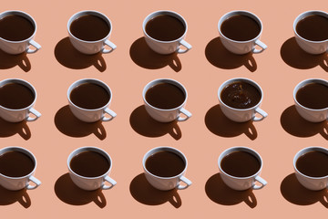 White cups with black coffee on a beige background. pattern with hard light. A splash of coffee in one cup.