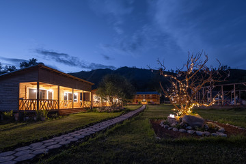 Wooden houses, beautiful tree with lights at night time in mountains hotel resort