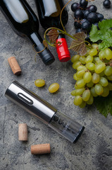 Electric metal corkscrew, grapes, two wine bottles and wine corks. On a gray concrete background. View from above