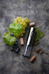 Electric metal corkscrew, grapes and wine corks. On a gray concrete background. View from above
