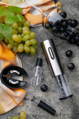 Electric metal corkscrew, wine aerator and vacuum stopper. On a gray concrete background. Nearby lies a glass and grapes, Top view.