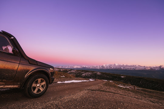 Offroad car traveling in mountains, road to amazing pink sunset view wit snow mountains skyline