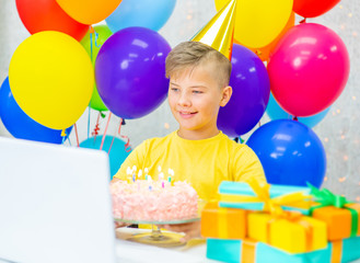 Fototapeta na wymiar Smiling boy wearing party's cap celebrating birthday on video call during the coronavirus epidemic