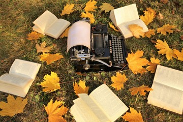 Reading and writing a book concept. Book publishing.World Book Day. Autumn Writing Marathon.NaNoWriMo.Vintage typewriter and yellow maple leaves in the grass.Fall time. Autumn mood