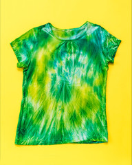 Yellow and green tie dye t-shirt with short sleeves on a yellow background. Flat lay.