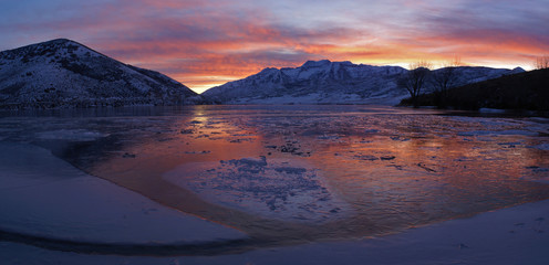 Deer Creek reservoir is frozen over and the sunset reflects in it's ice covered surface as mount timpanogos looms in the distance.