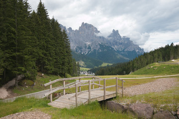 Fototapeta na wymiar Panoramic view of little wooden bridge and Pale di San Martino in San Martino di Castrozza, Trentino