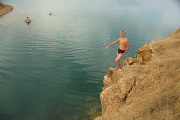 Teenager on rocky shore before swimming in blue, clear lake