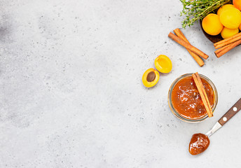 Apricot jam in a glass jar, fresh apricots, thyme and cinnamon on grey background.
