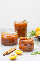 Homemade organic apricot jam in glass jars, ripe apricots, cinnamon and thyme on grey background.