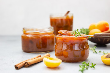 Homemade organic apricot jam in glass jars, ripe apricots, cinnamon and thyme on grey background.