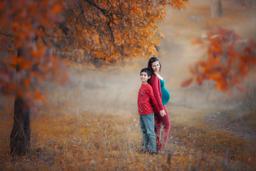 Pregnant woman with boy in the autumn forest. Mother and son. Autumn family portrait. Pregnancy, maternity, expectation concept. Beautiful tender mood photo of pregnancy.