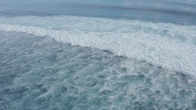 Aerial view of transparent clear blue waves of the sea splashing ashore from one after another. Concept of relaxation in the warm tropical country. Slow Motion footage