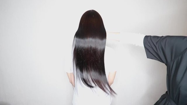 A hairdresser demonstrates the result after lamination and straightening of hair in a beauty salon for a girl with brown hair. hair care concept. Keratin hair treatment