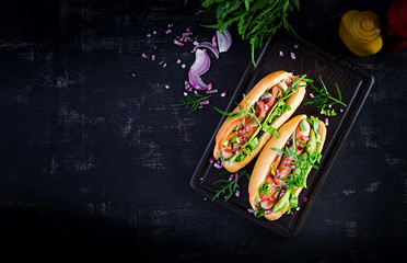 Hot dog with sausage, cucumber, tomato and red onion on dark background. Top view. Flat lay. Copy...