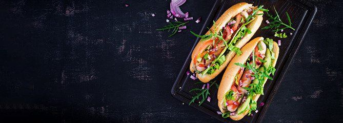 Hot dog with sausage, cucumber, tomato and red onion on dark background. Top view. Flat lay. Copy...