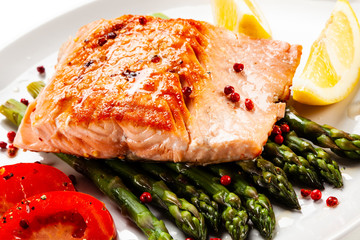 Fried salmon fillet with asparagus, lemon and tomatoes on white background
