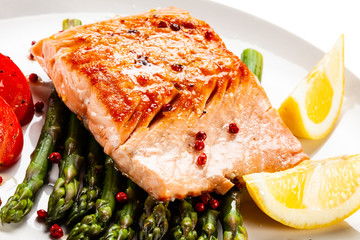 Fried salmon fillet with asparagus, lemon and tomatoes on white background
