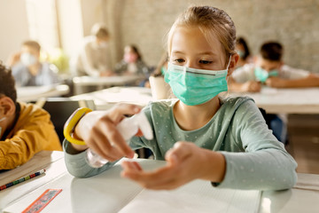 Schoolgirl with face mask using hands sanitizer in the classroom.