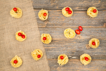 Nests of tagliatelle noodles with egg-shaped mini roma tomatoes on a rustic wooden table with burlap