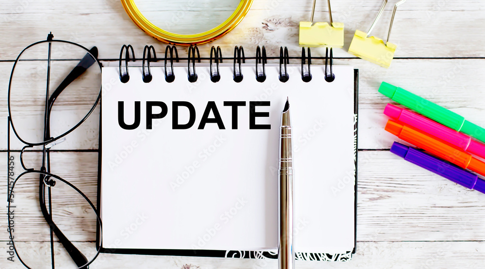 Aufkleber update written in a notebook on white background with office tools