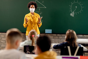 Fototapeta African American elementary teacher wearing face mask while giving a lecture to her students in the classroom. obraz