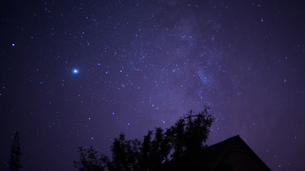 Starry night sky and the milky way against the background of a tree and the roof of a house at...