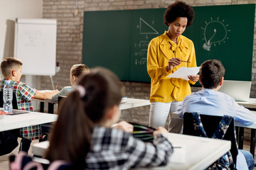 Black teacher explaining a lesson to elementary students in the classroom.