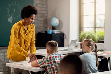 African American teacher assisting her students on on a class at elementary school.