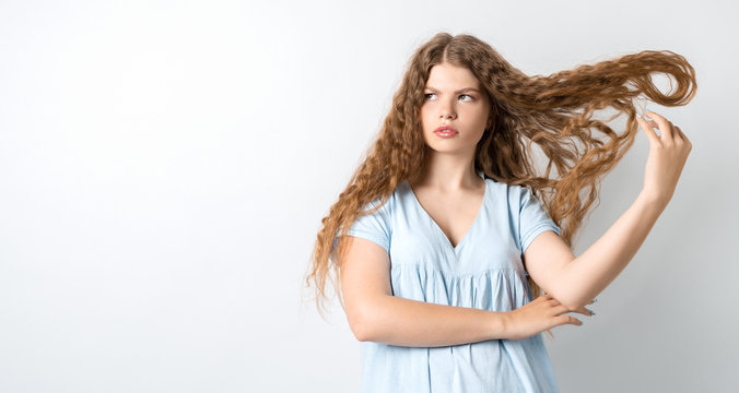 Portrait of attractive european girl, discontentedly tilting head and shaking curly hair. Copy space for your text
