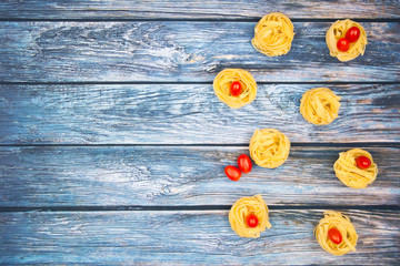 Nests of tagliatelle noodles with egg-shaped mini roma tomatoes  on a weathered bluish table. With copy space.