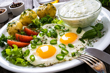 The best summer dinner - sunny side up eggs, boiled potatoes, cucumbers in yogurt  and fresh vegetables served on wooden table
